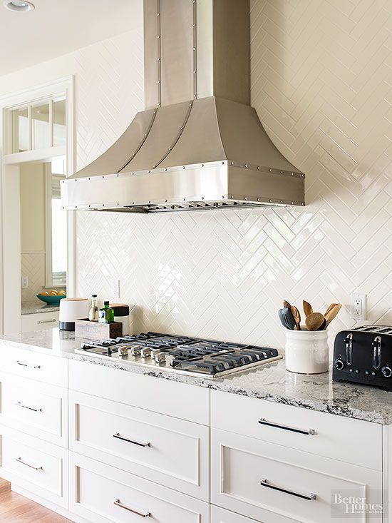 a stylish white kitchen with shaker cabinets, white countertops, a white herringbone tile backsplash and stainless steel appliances