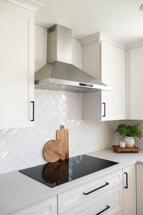 a white farmhouse kitchen with a white herringbone tile backsplash and white countertops, black handles is amazing