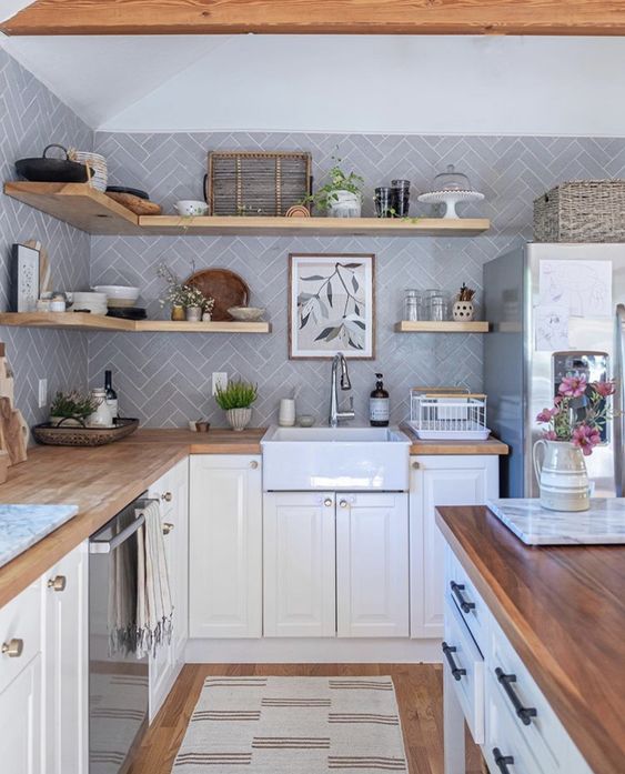 a white farmhouse kitchen with pale blue herringbone tile walls, open shelves and lots of greenery is cool
