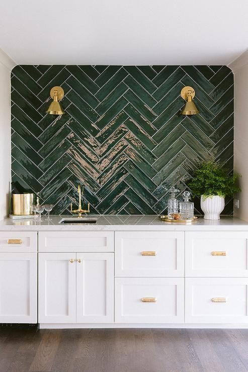 a white kitchen with a glossy herringbone green backsplash and brass and gold touches for a super elegant and glam look