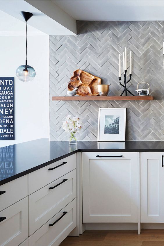 a white kitchen with lower white cabinets, black countertops, grey herringbone tiles on the wall and open shelving