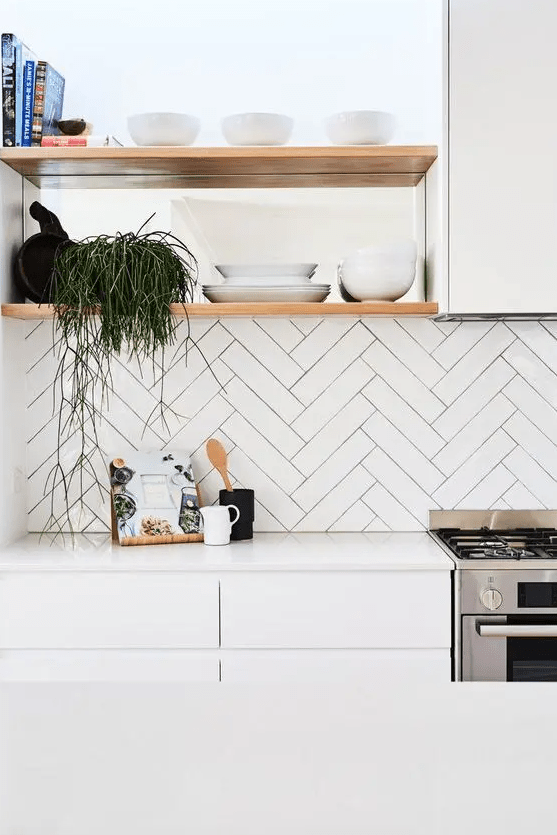 a white minimalist kitchen with a herringbone tile backsplash, open shelves and a sleek white kitchen island, some greenery