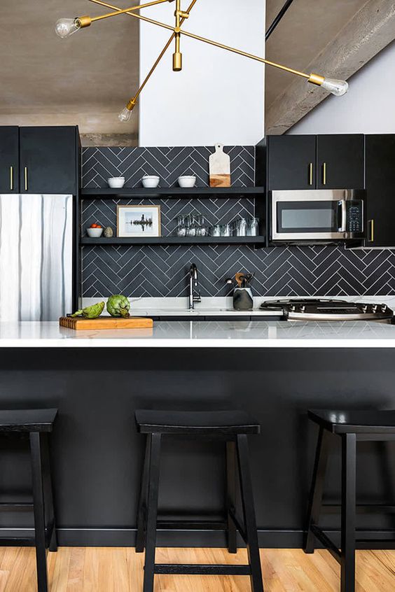 an elegant black kitchen with white countertops and a black herrignbone backsplash with white grout plus brass touches
