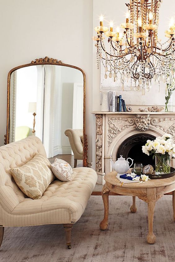 a refined vintage living room with an ornated fireplace, exquisite furniture, an oversized mirror in a gilded frame and a chic chandelier
