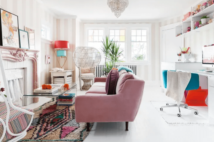 a colorful eclectic living room with quriky furniture and a workspace with a desk, open shelves and a cabinet