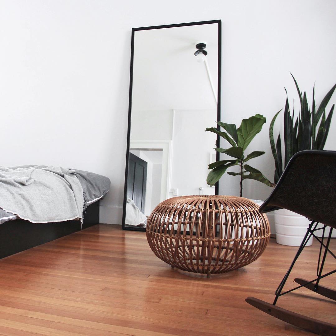 a modern boho bedroom with a black bed and chair, an oversized mirror in a simple black frame and potted plants
