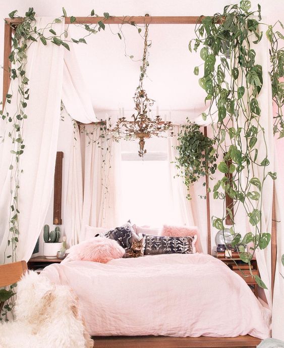 a boho-inspired bedroom with mid-century modern furniture, white curtains and greenery on the canopy bed and pink bedding
