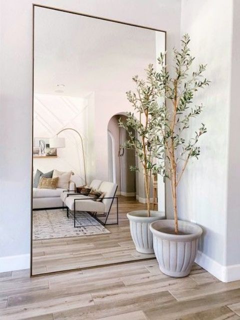 a neutral and chic farmhouse living room with a laconic oversized mirror in a brass frame plus a potted tree is cool