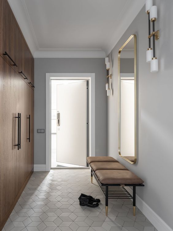 a laconic and minimal entryway with an oversized mirror with a gilded frame, a leather bench and sleek wardrobes
