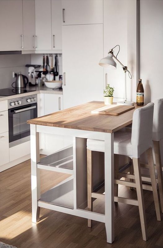 a stylish contemporary kitchen in white with neutral countertops, a small kitchen island that doubles as an eating zone