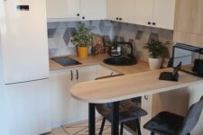 a Scandinavian kitchen with sleek white cabinets,a mosaic tile backsplash, a breakfast bar and tall grey stools plus potted greenery