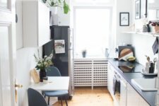 a Scandinavian kitchen with white cabinets and black countertops, a black fridge, a wall-mounted breakfast bar, navy chairs