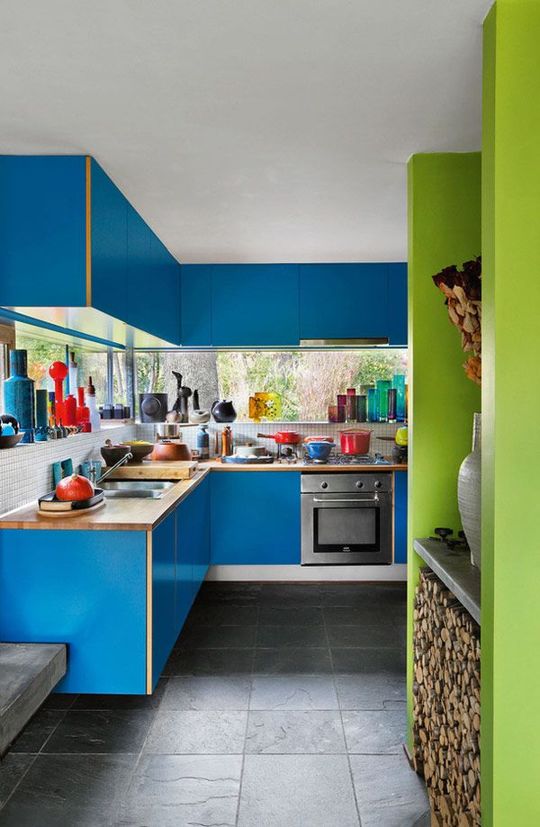 a bold kitchen with electric blue cabinets, butcherblock countertops and a green storage unit with fireplace