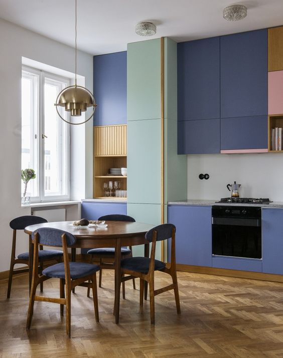 a bright kitchen with purple, pink and mint green sleek cabinets, stained wooden items and a stained table with navy chairs
