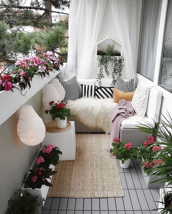 a bright summer balcony with a corner bench, potted blooms and greenery, paper lamps and a small coffee table