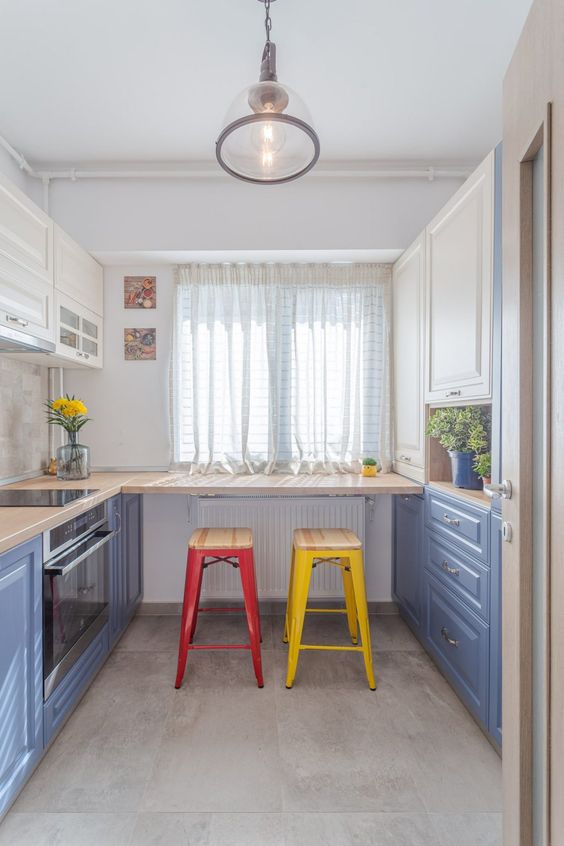 a colorful kitchen with cobalt blue and white cabinets, a breakfast bar with colorful stools, a pendant lamp and potted greenery