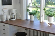a farmhouse windowsill breakfast bar with drawers, tall black stools, a chalkboard and pendant lamps plus a view