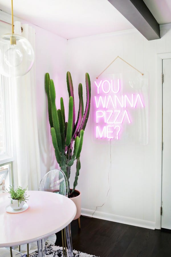 a glam modern dining space with a blush table and a pink neon sign that gives a quirky touch to the space