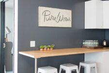 a graphite grey kitchen with sleek white cabinets, a breakfast bar, tall white stools, artwork and cool decor