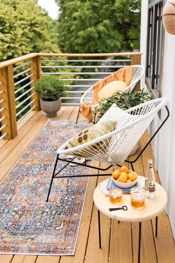 a lovely summer balcony with white round chairs, a boho rug, a small side table and potted greenery is amazing