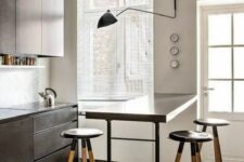 a modern black kitchen with sleek cabinets, a breakfast bar, tall stools and a black sconce is a bold and chic space