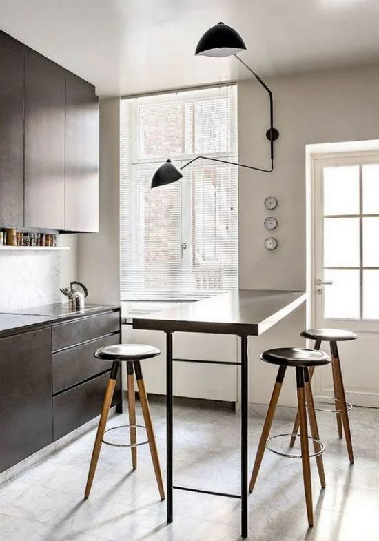 a modern black kitchen with sleek cabinets, a breakfast bar, tall stools and a black sconce is a bold and chic space