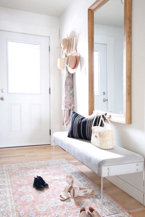 a modern light filled entryway with a bench with acrylic legs, a statement mirror, a boho rug and a clothes rack