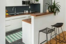 a modern white kitchen with sleek cabinets, a black chalkboard backsplash, a raised breakfast bar and black stools
