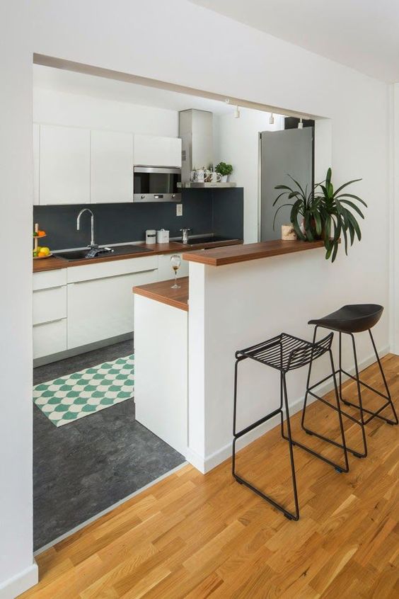 a modern white kitchen with sleek cabinets, a black chalkboard backsplash, a raised breakfast bar and black stools