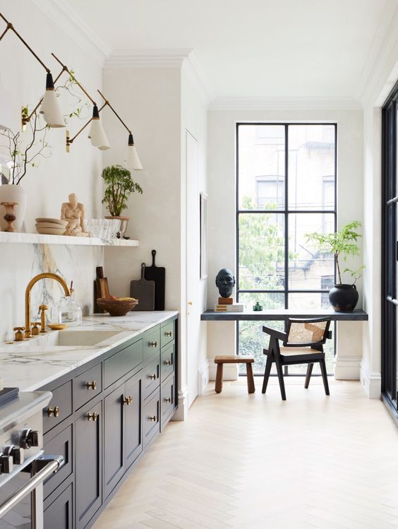 a navy contemporary kitchen with a white stone countertop and a backsplash, a floating shelf and sconces plus a small workspace by the window with a built-in desk