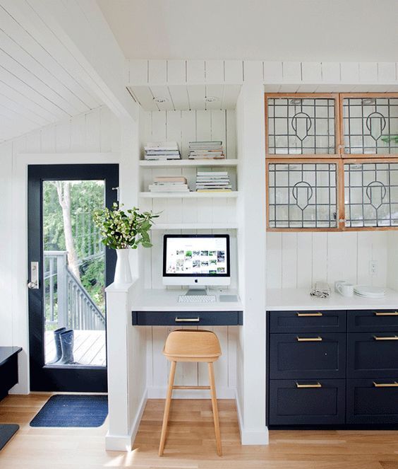 a navy farmhouse kitchen with a white backsplash and glass cabinets, a tiny workspace nook with built-in shelves and a drawer-style desk plus a stool