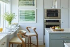 a pale blue kitchen with a large kitchen island, a windwosill breakfast bar with storage, elegant stools and some artwork