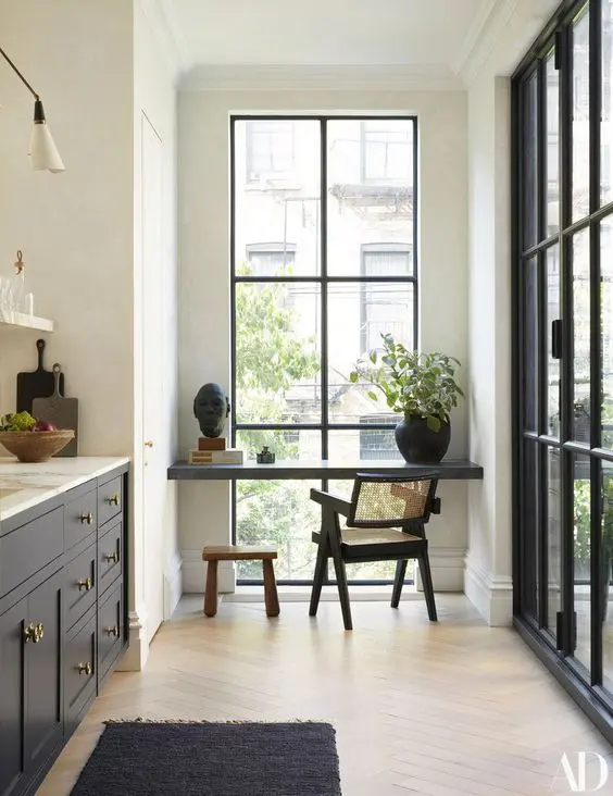 a refined kitchen with black cabients and white marble countertops, a black windowsill breakfast bar and greenery