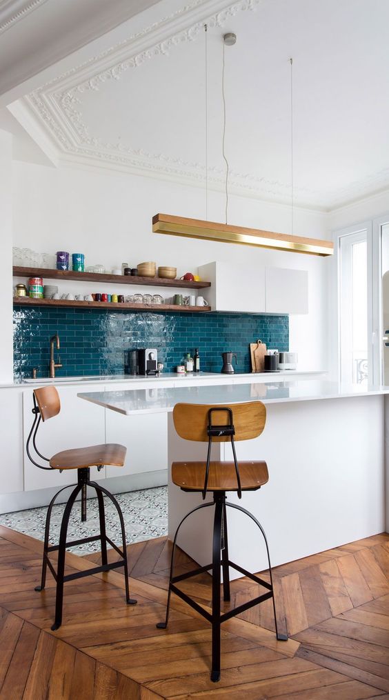 a sleek and modern white kitchen with a blue tile backsplash, a kitchen island with a breakfast bar, tall stools