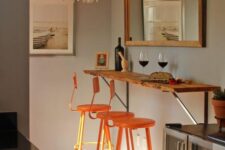 a small and chic breakfast bar with a mirror, a living edge breakfast bar, orange stools, a chic chandelier