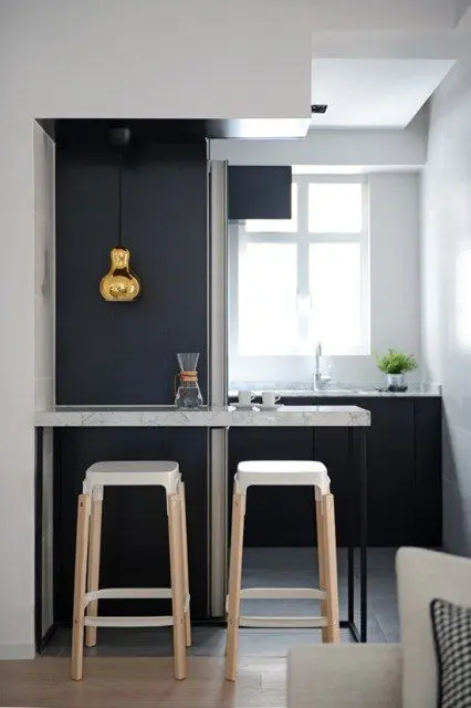 a small black and white kitchen with a breakfast bar, tall stools, a gold pendant lamp is a lovely space with everything necessary