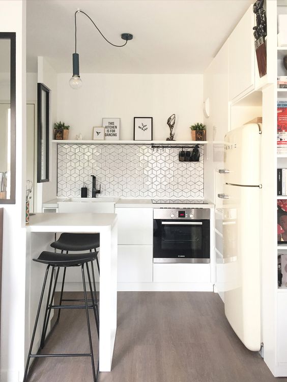 a tiny white kitchen with a geometric tile backsplash, a small breakfast bar, black stools and a shelf with decor