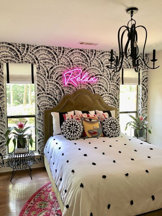 a whimsical bedroom with a printed wallpaper wall, an upholstered bed, mismatching nightstands and a neon light over the bed
