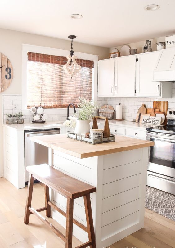 a white farmhouse kitchen with a small kitchen island that includes a breakfast bar, a wooden bench and a pendant lamp