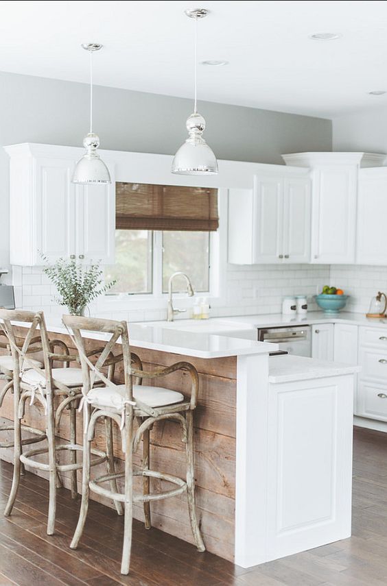 a white farmhouse kitchen with a subway tile backsplash, a raised breakfast bar, vintage stools and pendant lamps