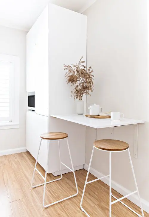 a white minimal kitchen with built-in appliances, a small breakfast bar, tall stools is a cool and chic space