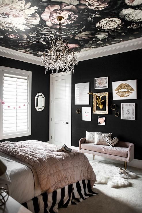 a refined bedroom with black walls, a black floral wallpaper ceiling, a crystal chandelier and blush and gold touches