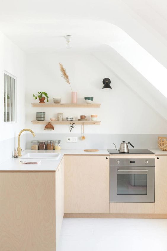 a Scandinavian attic kitchen with light stained plywood cabinets, white countertops, open shelves, a skylight and gold touches
