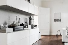 a Scandinavian space with dark stained parquet flooring, sleek white cabinets, white furniture and some art and accessories