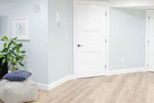 a basement space with vinyl flooring that imitates stained wood, light blue walls and some ottomans is welcoming