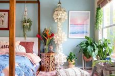 a boho summer bedroom with a canopy bed, a printed rug, pink and blue bedding, potted plants, a mother of pearl chandelier