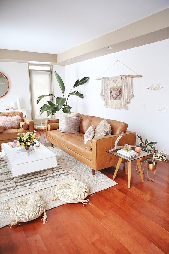 a boho summer living oom with amber sofas, a low coffee table, woven poufs, a macrame piece and some potted plants