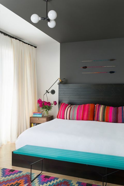 a bold summer bedroom with a black bed, a grey accent wall and ceiling, colorful pillows and a rug and a turquoise bench