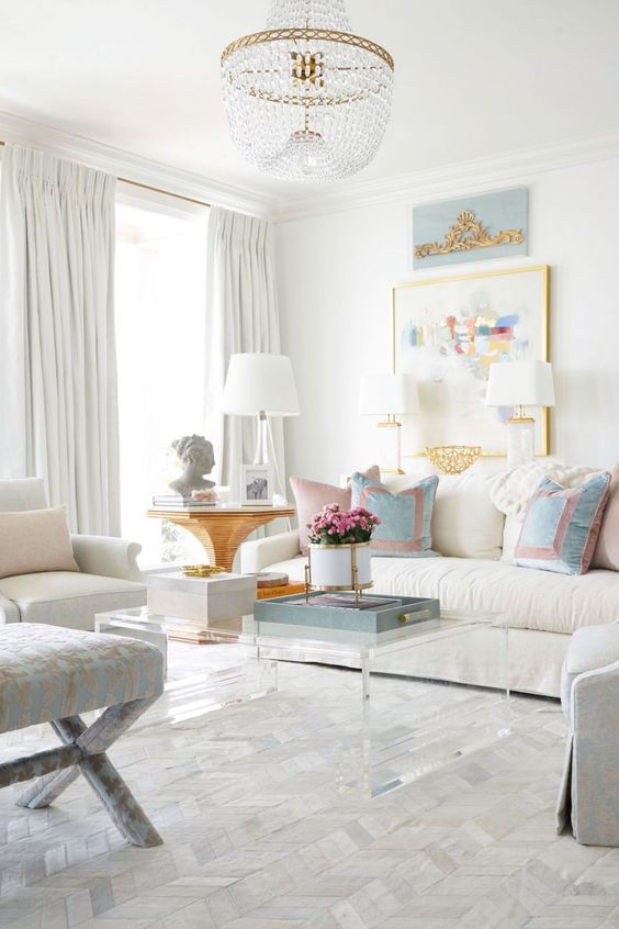 a breezy summer living room with white and grey furniture, pastel pillows and a lovely gallery wall, a crystal chandelier and an acrylic coffee table