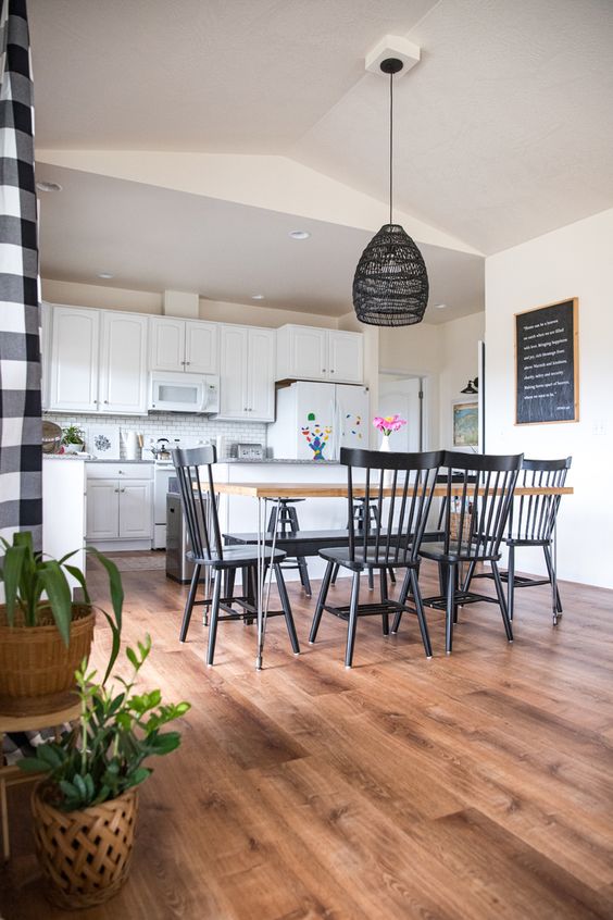 a chic farmhouse space with white walls and laminate looking vinyl, with white cabinets, a dining table and black chairs